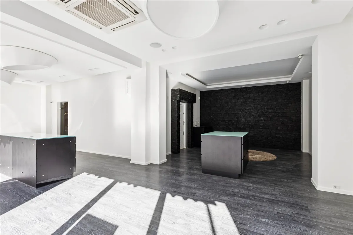 Minimalistisk og funktionel kontor med højt loft, to store sort/grå skriveborde, og et sort og gult murværk.