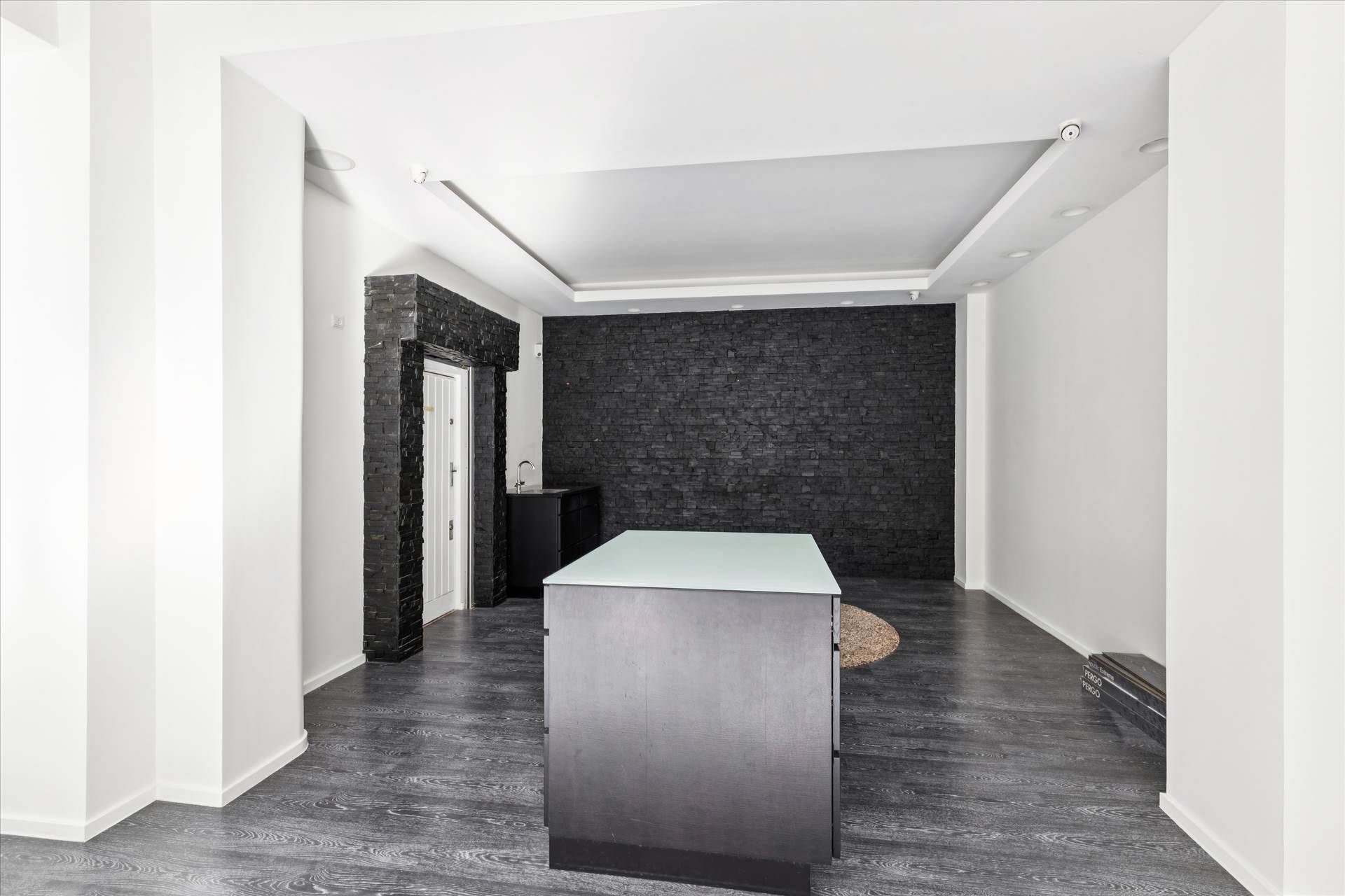 Minimalistisk interiør med høje hvide vægge og mørke gulvbelægning samt en stor glasadgangsdør og en sort væg med en hvid dør