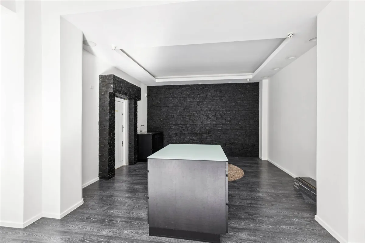 Minimalistisk interiør med høje hvide vægge og mørke gulvbelægning samt en stor glasadgangsdør og en sort væg med en hvid dør