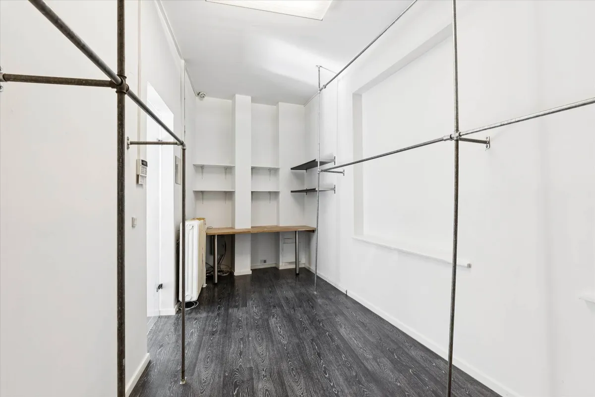 Indeni et minimalistisk og rensket værelse med hvide vægge og en mørk trægulv samt metalliske garderobebøjler