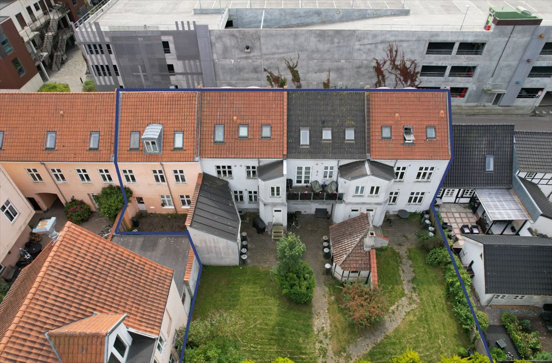 Fire ejendomme med forskellige farver og stilarter ligger på Sundegade, med en have og terrasse i midten