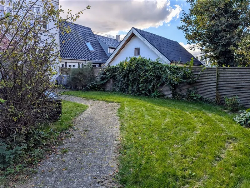 En smuk grøn have med sti og hæk, og bagved en hyggelig hvid villa med blå tag og store ruder