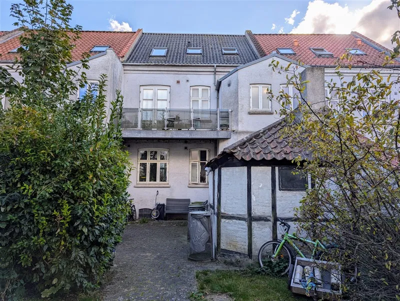 To-etages gårdhave med terrasse, have og fiksere. Gårdhave med bænk, cykel, skraldspande og rækværk