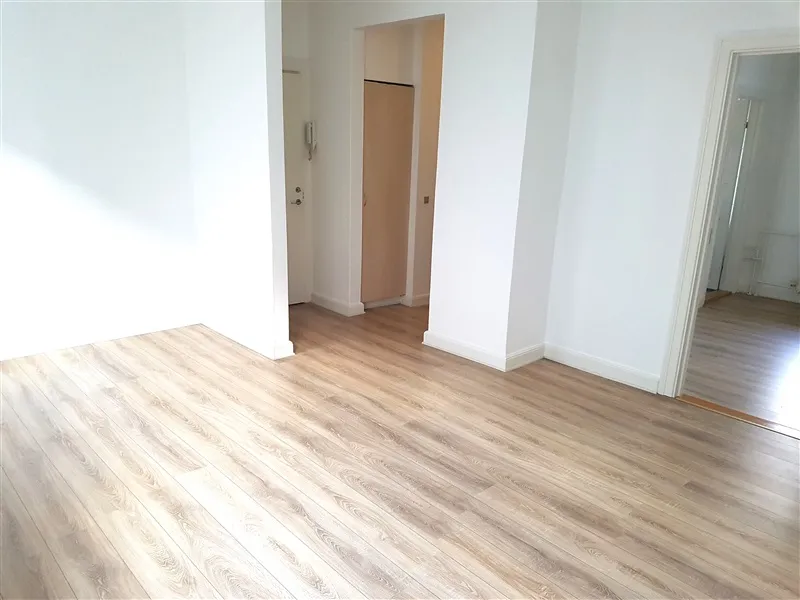 Et rum med hvide vægge og en trægulv i hvidt. Der er to døre, hvoraf den ene er åben og har en telefonhænger på væggen.