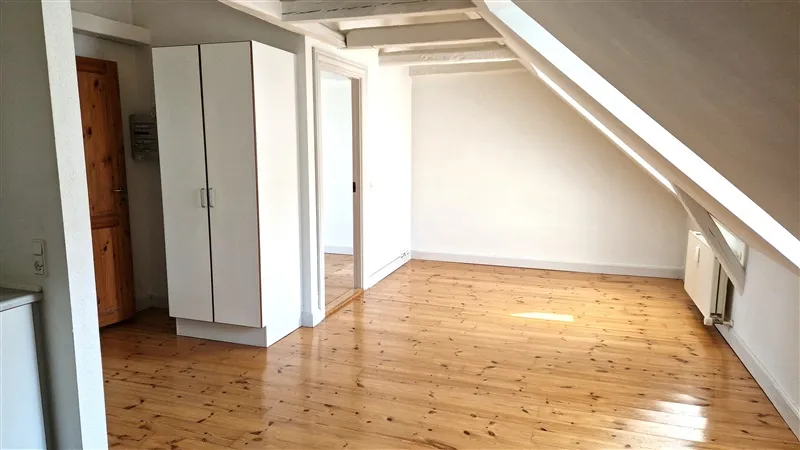 Loftsværelse med højloft, lyse trægulve, lyse vægge og en hvid garderobe samt træskabsdør