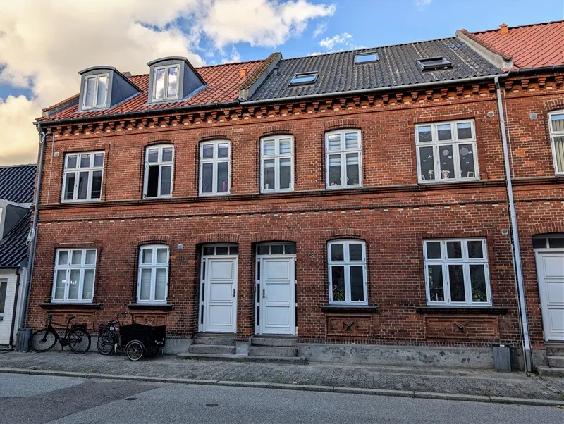 Fire etagers ejendomme med to hvide døre og fire vinduer pr etage med røde tag og to cykler foran