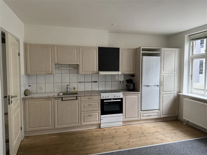 Alt-tekst: Et moderne køkken med lyse bøgeskabe og en hvid køleskab samt en komfur og ovn i hvidt.