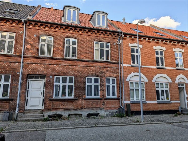 Fire lejligheder i et rødt murstenshus med hvide vindueskarme og røde tagdækninger.