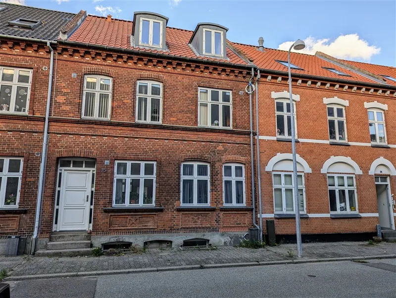 Fire lejligheder i et rødt murstenshus med hvide vindueskarme og røde tagdækninger.