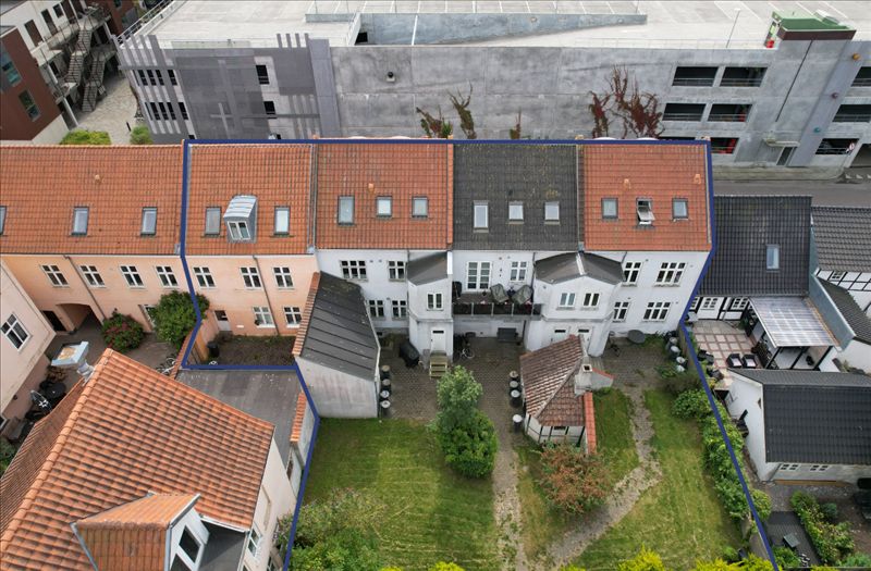 Fire rækkehuse med røde tag, hver med mange vinduer og små haver og parkeringspladser.