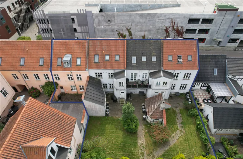 Fire rækkehuse med røde tag, hver med mange vinduer og små haver og parkeringspladser.