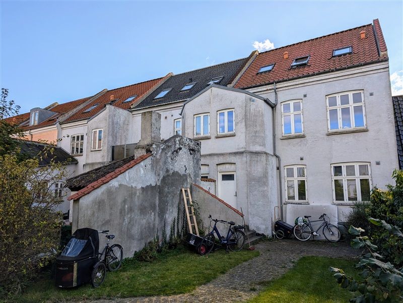 Fire huse med mange vinduer og røde tag og flere cykler og et køretøj parkeret udenfor