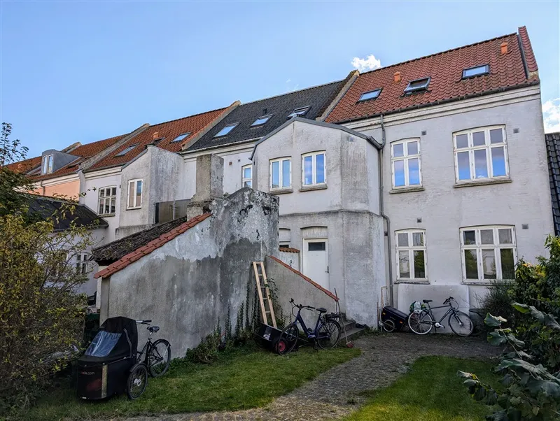 Fire huse med mange vinduer og røde tag og flere cykler og et køretøj parkeret udenfor