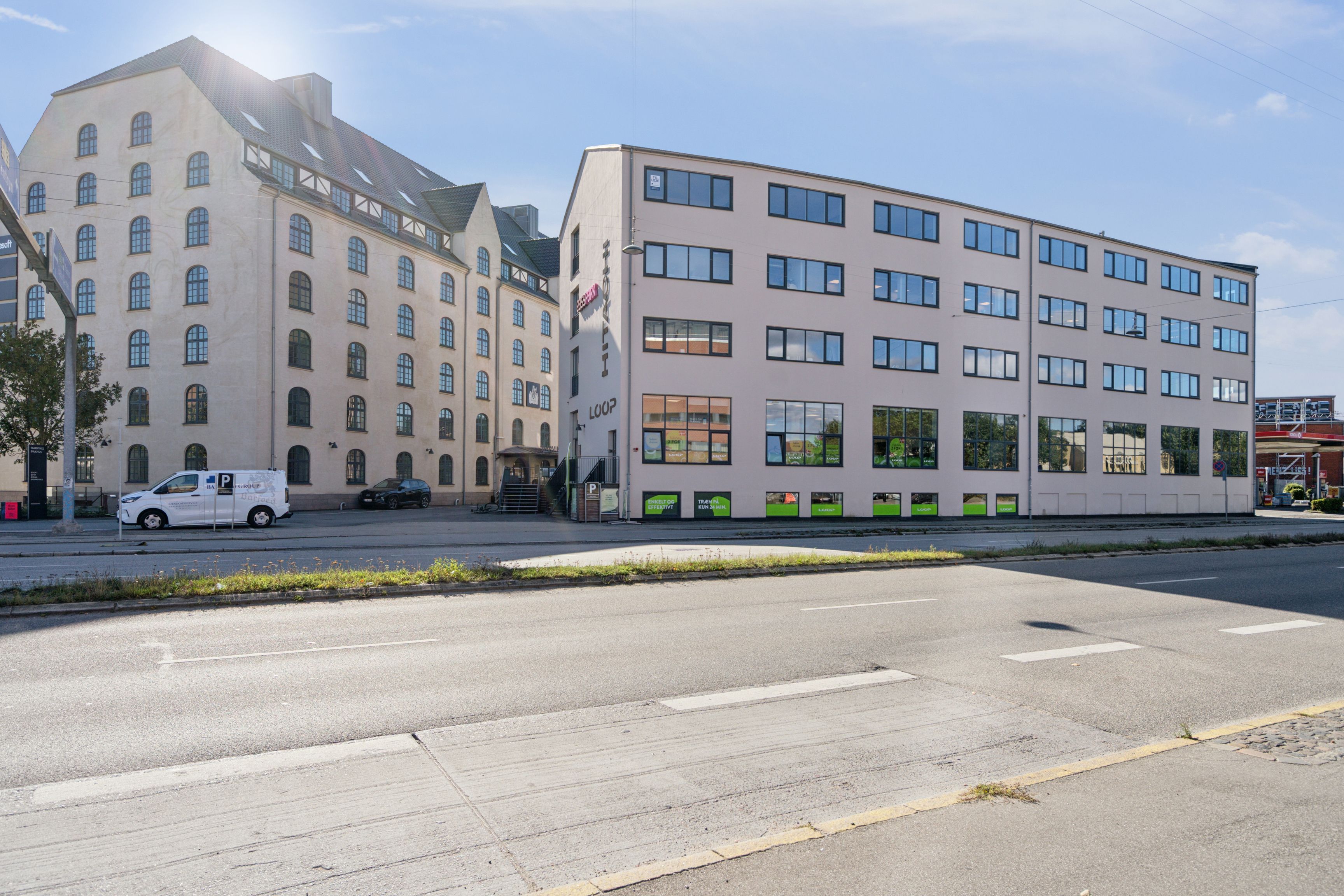 Kontorbyggeri med lyse vinduede lokaler, en parkeringsplads med en parkeringsplads og en bil, og en vej med hvide streger og