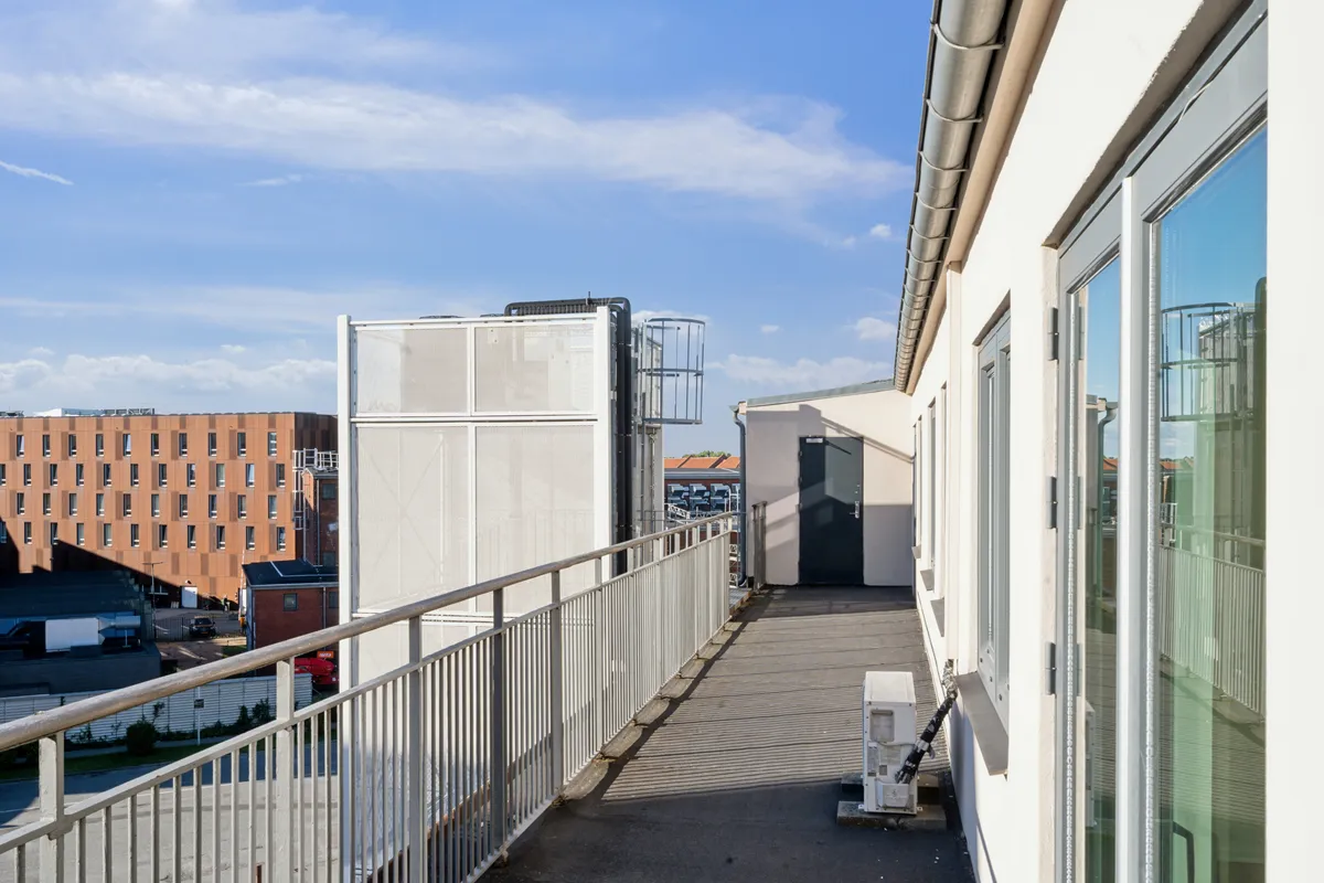 Kontorloft med tagterrasse og udsigt til bygninger og parkeringsplads under en skyet himmel
