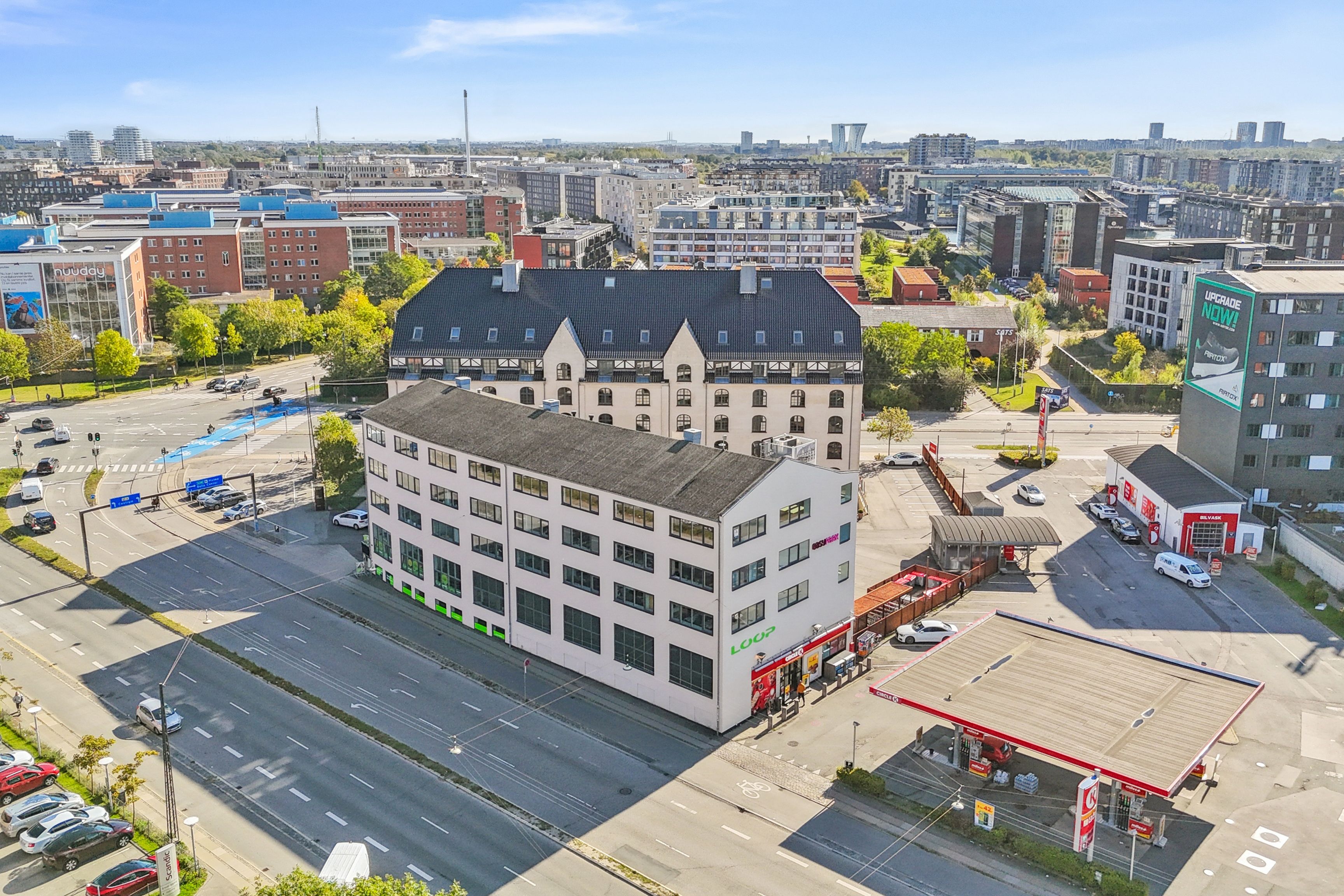 Moderne bygning med kontorer og tagterrasse, nær metro, S-tog, bus, parkering og motorvej, med reklameskilte og biler