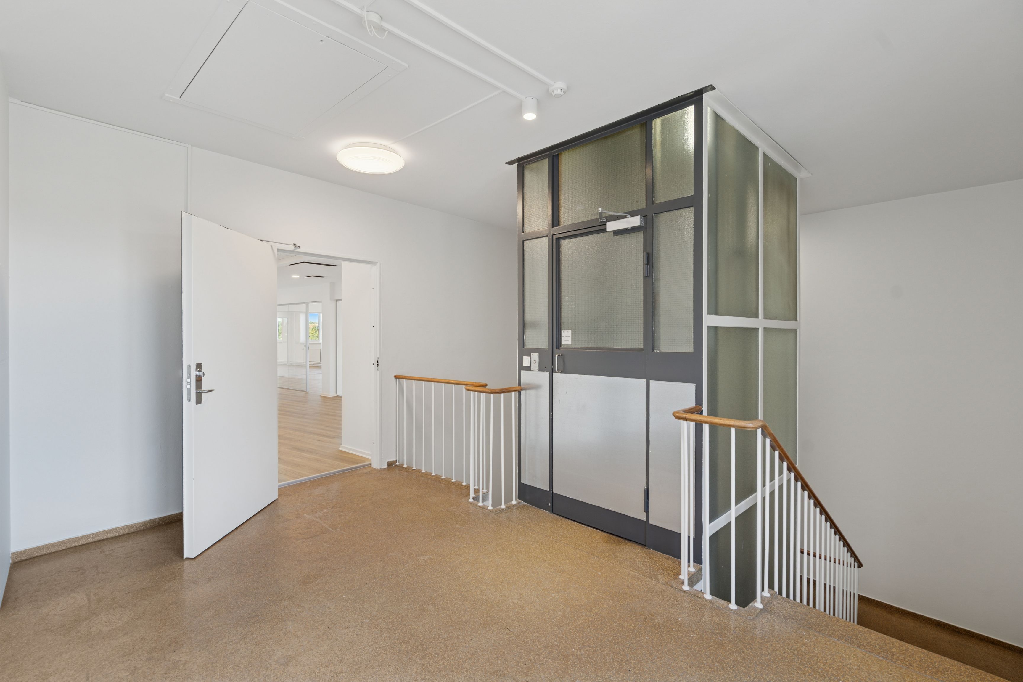 Et elegant og moderne kontorlokal med lyse lofter og hvidvaskede vægge. En slank elevator med glasdøre og et moderne