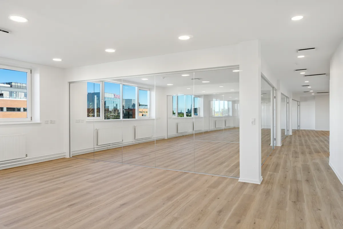 Lyst og rummeligt kontor med udsigt til byen og store vinduer. Store spejl og moderne design giver en følelse af rummelighed