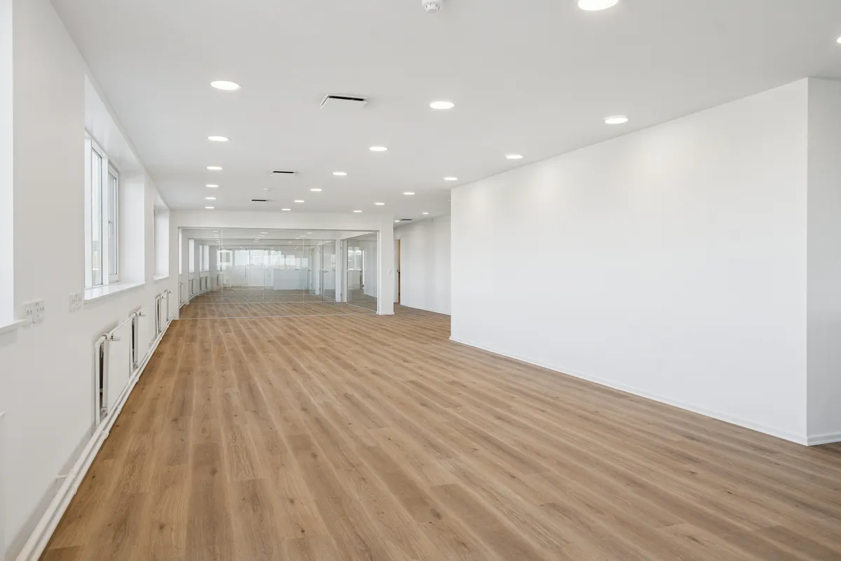 Hvidt kontorlokal med lysegul gulvbelægning og hvide vægge, glasdøre, vinduer, hvide radiatorer og rundt lys i loftet