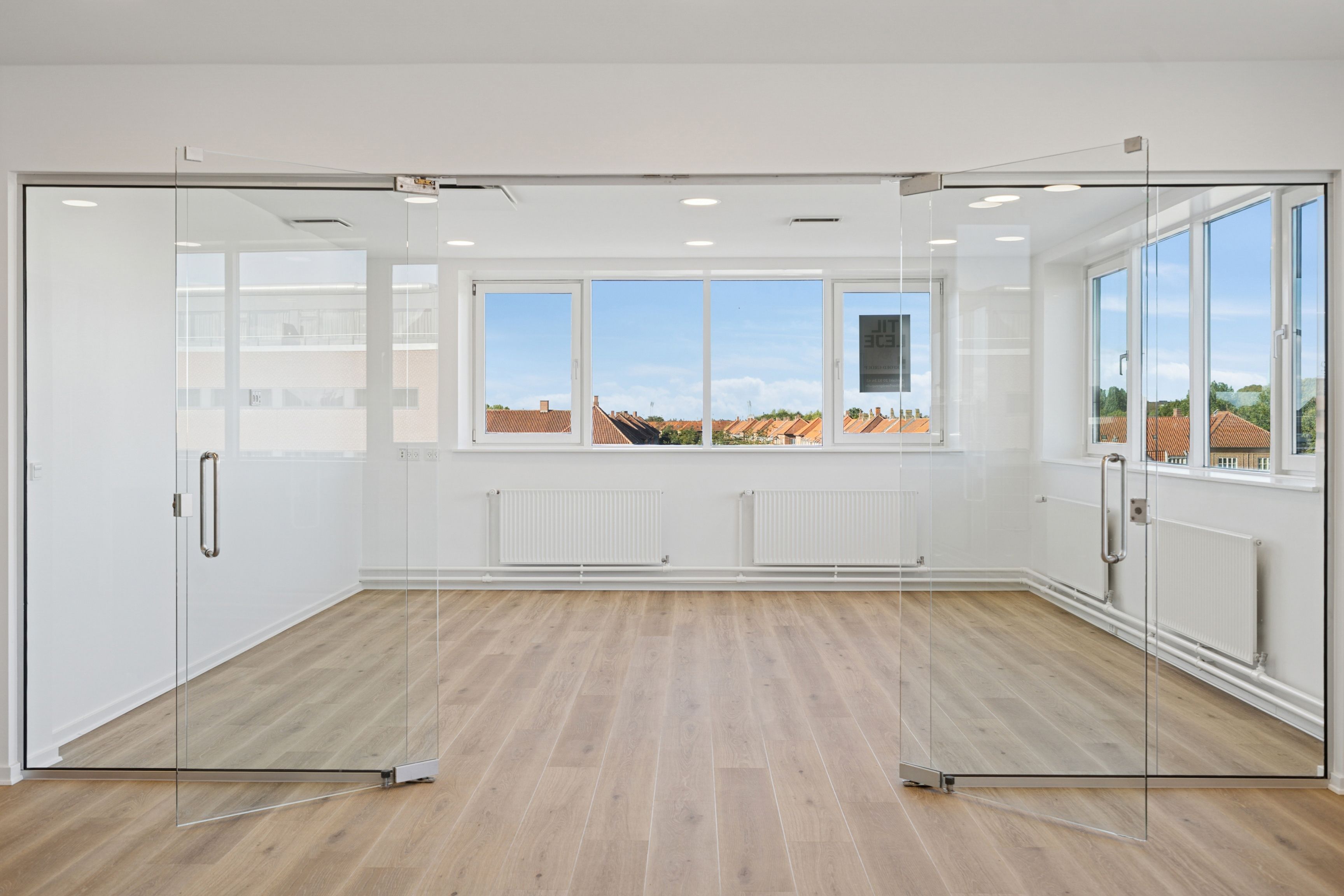 En stor og glasklat kontorvand med højt loft og moderne radiatorer samt vinduer med udsigt til byen og himlen