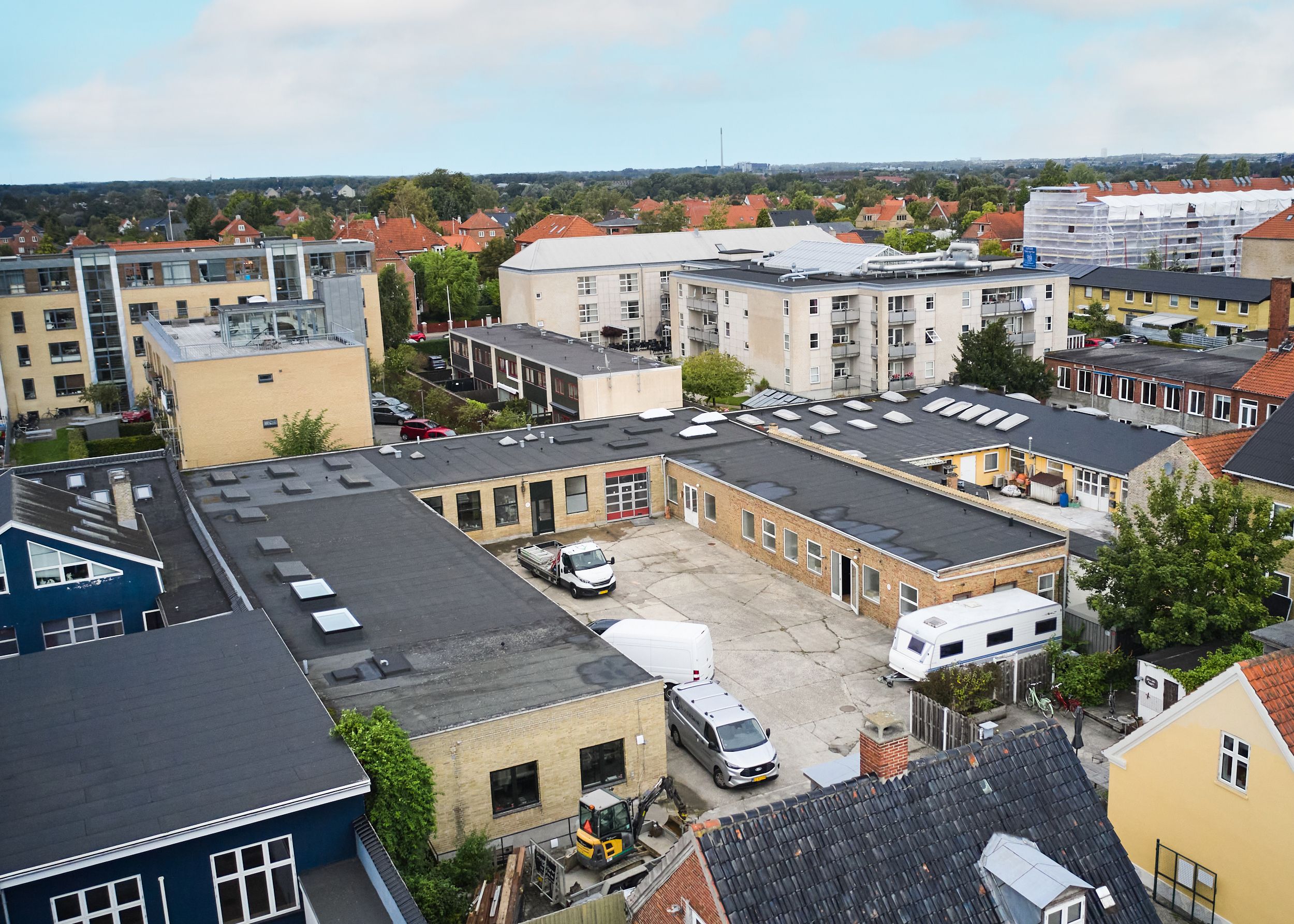 En luftfoto af et stort byggeområde med flere bygninger, hvor der er parkeringspladser og flere køretøjer