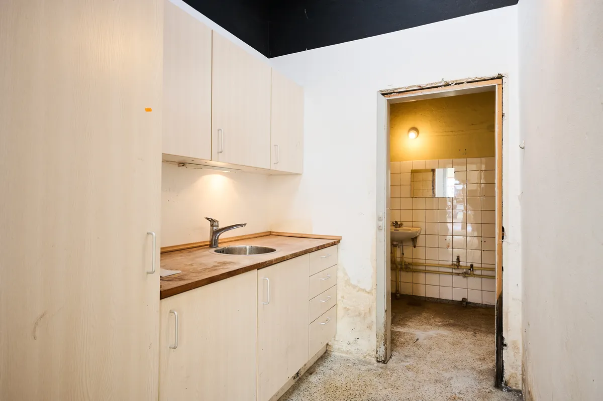 Et rum med åbne døre, hvor der er et træbord med en rustfri stålvask og vandhane samt hængende hvidt skab og en dør med en