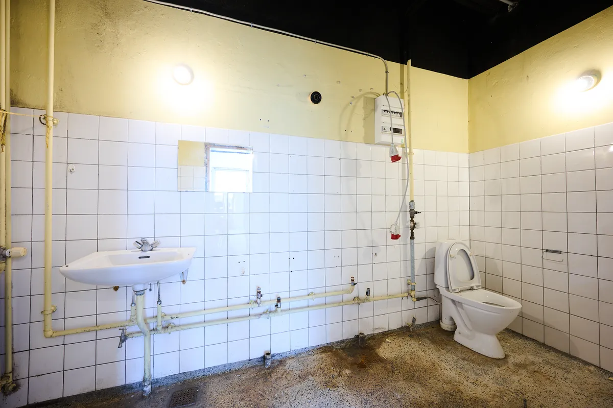 En lille toiletrum med to lys, et toilet, en hvid sænk og nogle rør i væggen