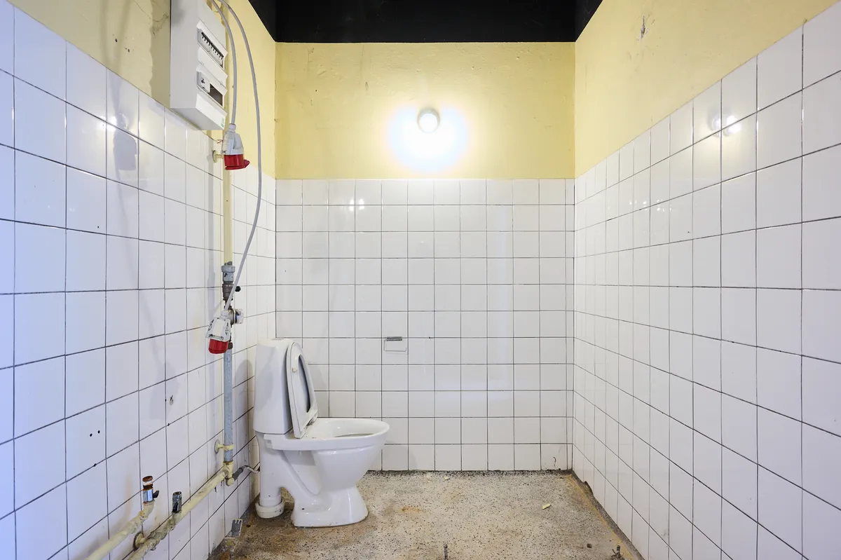 En tom, hvidt flisede toiletrum med toilet og vandforsyning samt en lysekronen i loftet