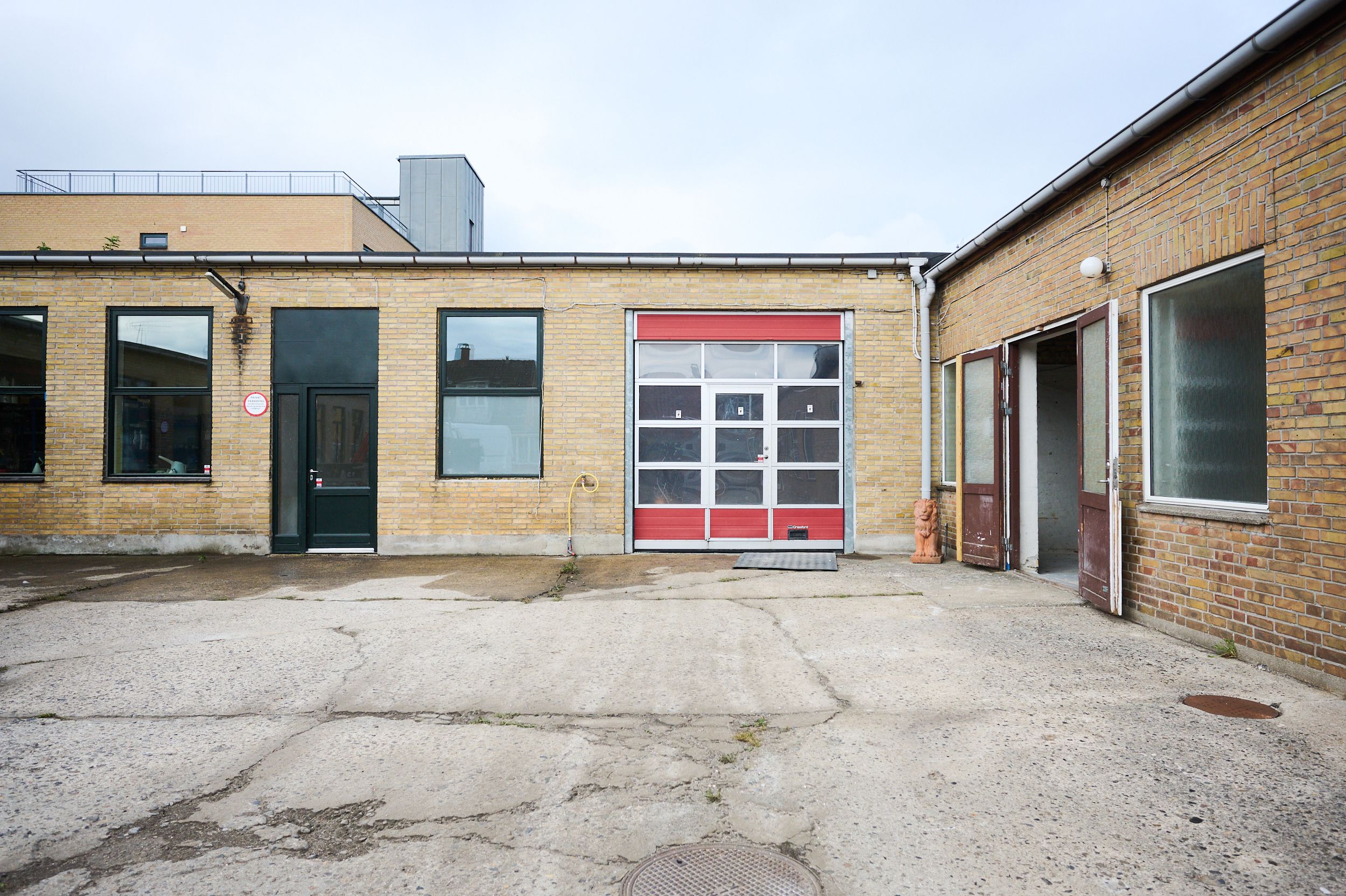 Rådgivende loftsværelser med garage og åbne døre i lyse, gule mursten. Alle lokaler har store vinduer og lyse lofter