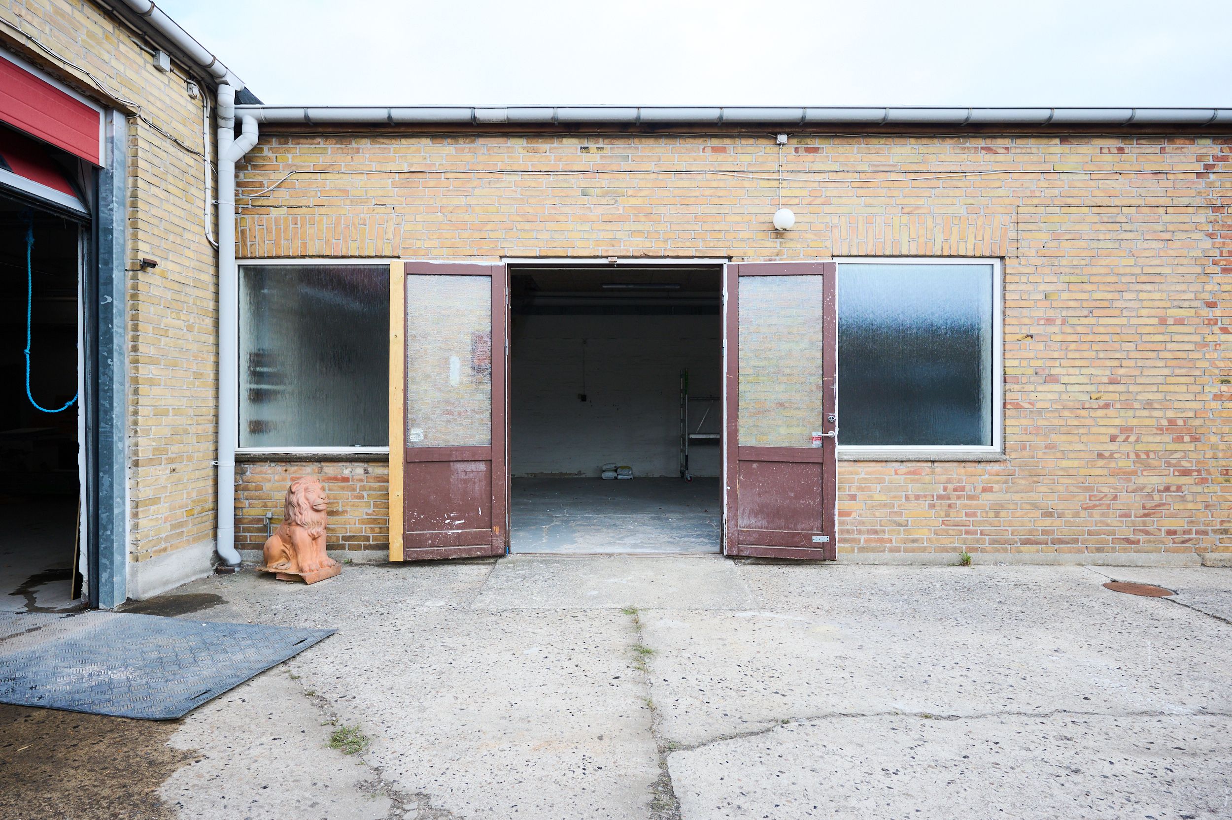 Store åbne døre til et renoveret værksted i røde mursten med en lysekronehylde og statue af en løve uden for