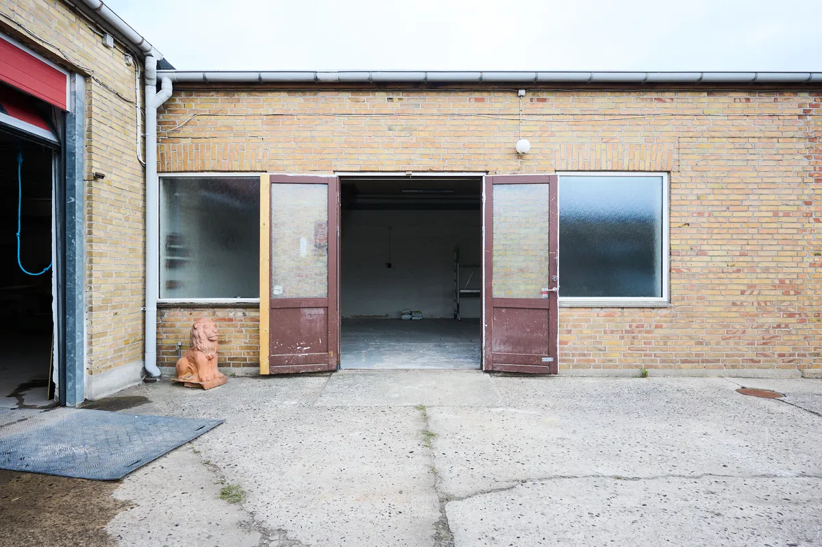Store åbne døre til et renoveret værksted i røde mursten med en lysekronehylde og statue af en løve uden for