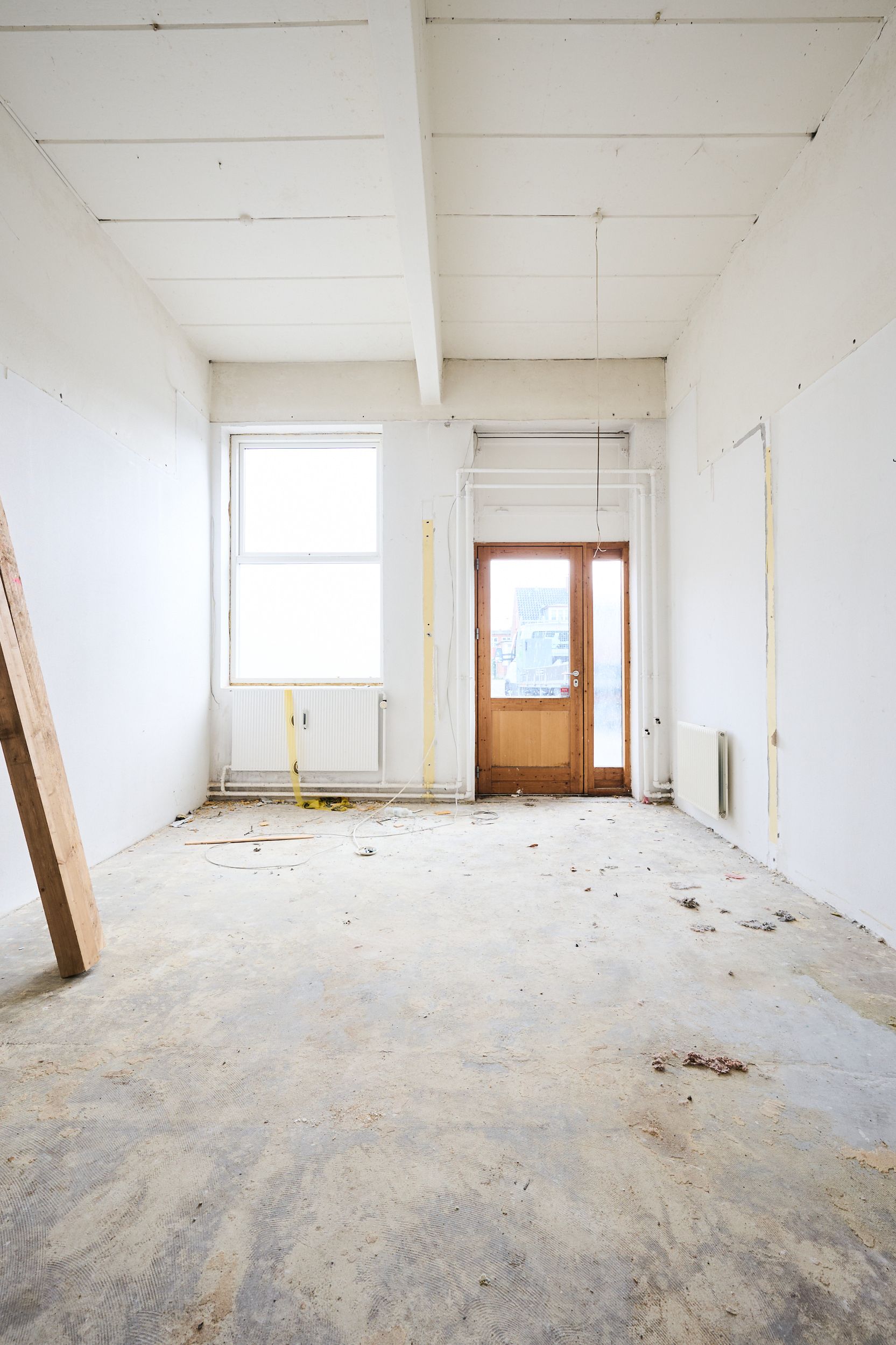 Tomme vægge med bjælker, gulv og loft, hvor der er snedkerværkstøj og gulvbelægning samt et vindue og en dør