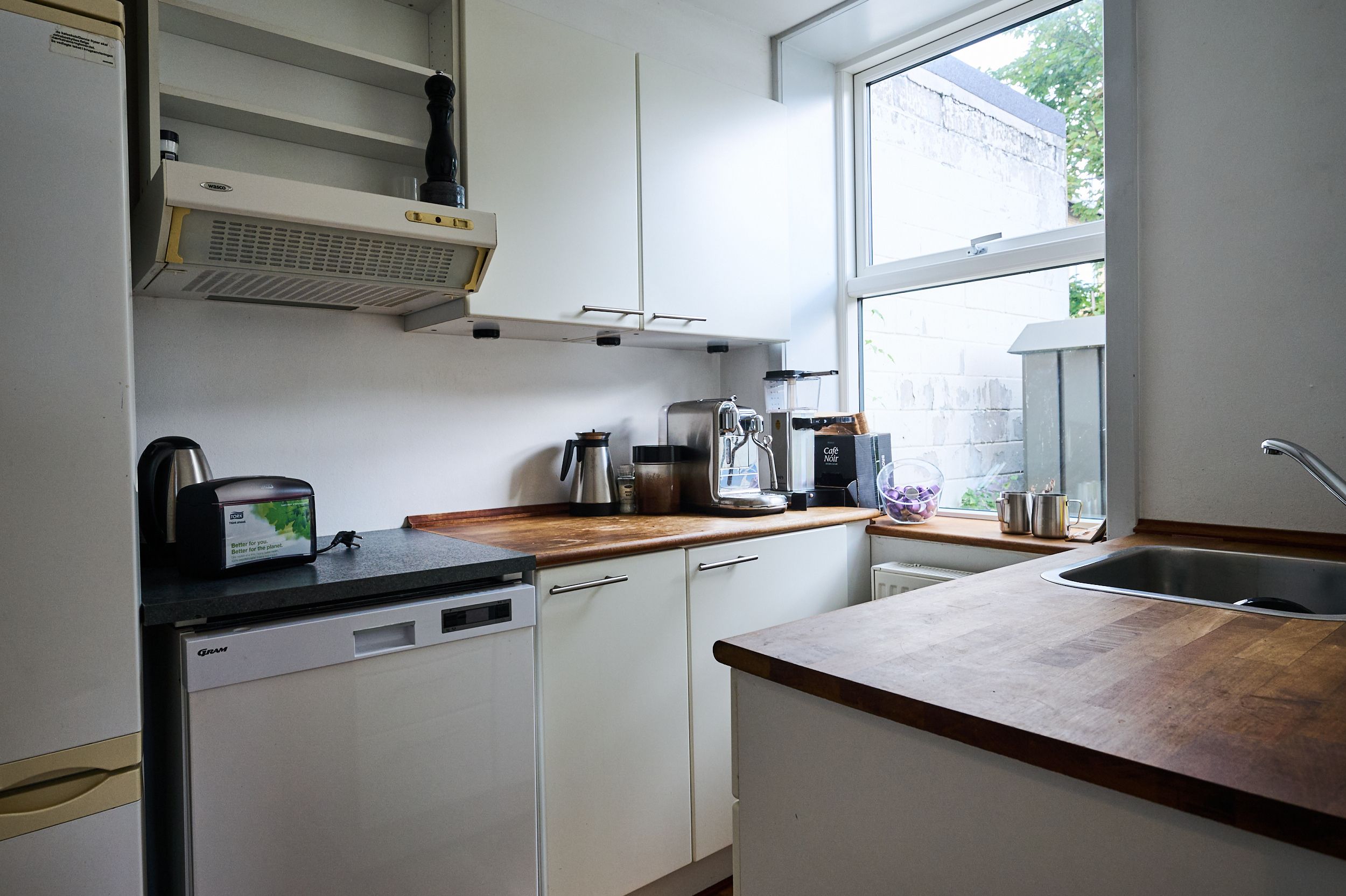 Hvid køkken med en ovn, en kaffemaskine, en mikrobølgeovn, en vaskemaskine og en tørretumbler på gulvet, et vindue og en