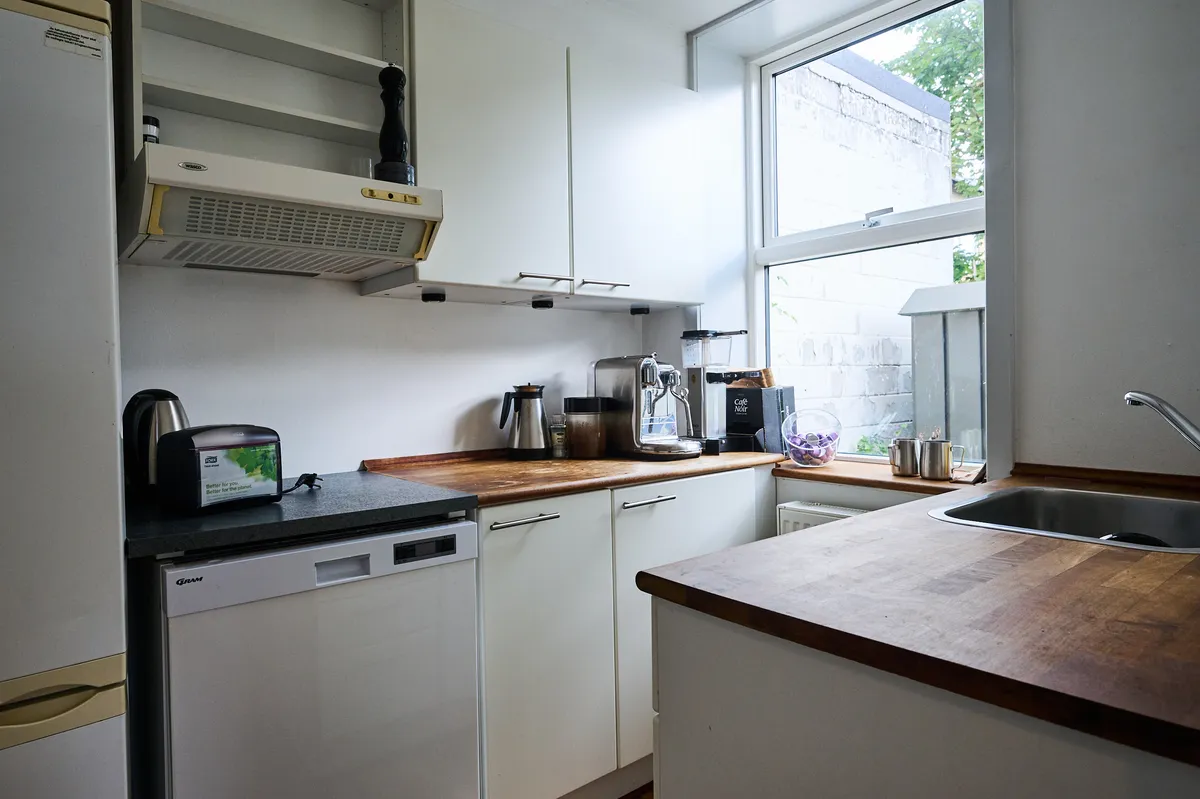 Hvid køkken med en ovn, en kaffemaskine, en mikrobølgeovn, en vaskemaskine og en tørretumbler på gulvet, et vindue og en