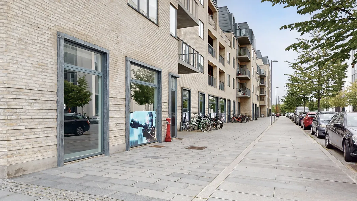 Nybygget erhvervslejemål med store vinduer og glasdøre i København. Adgangsvej med parkerede biler og cykler. Moderne