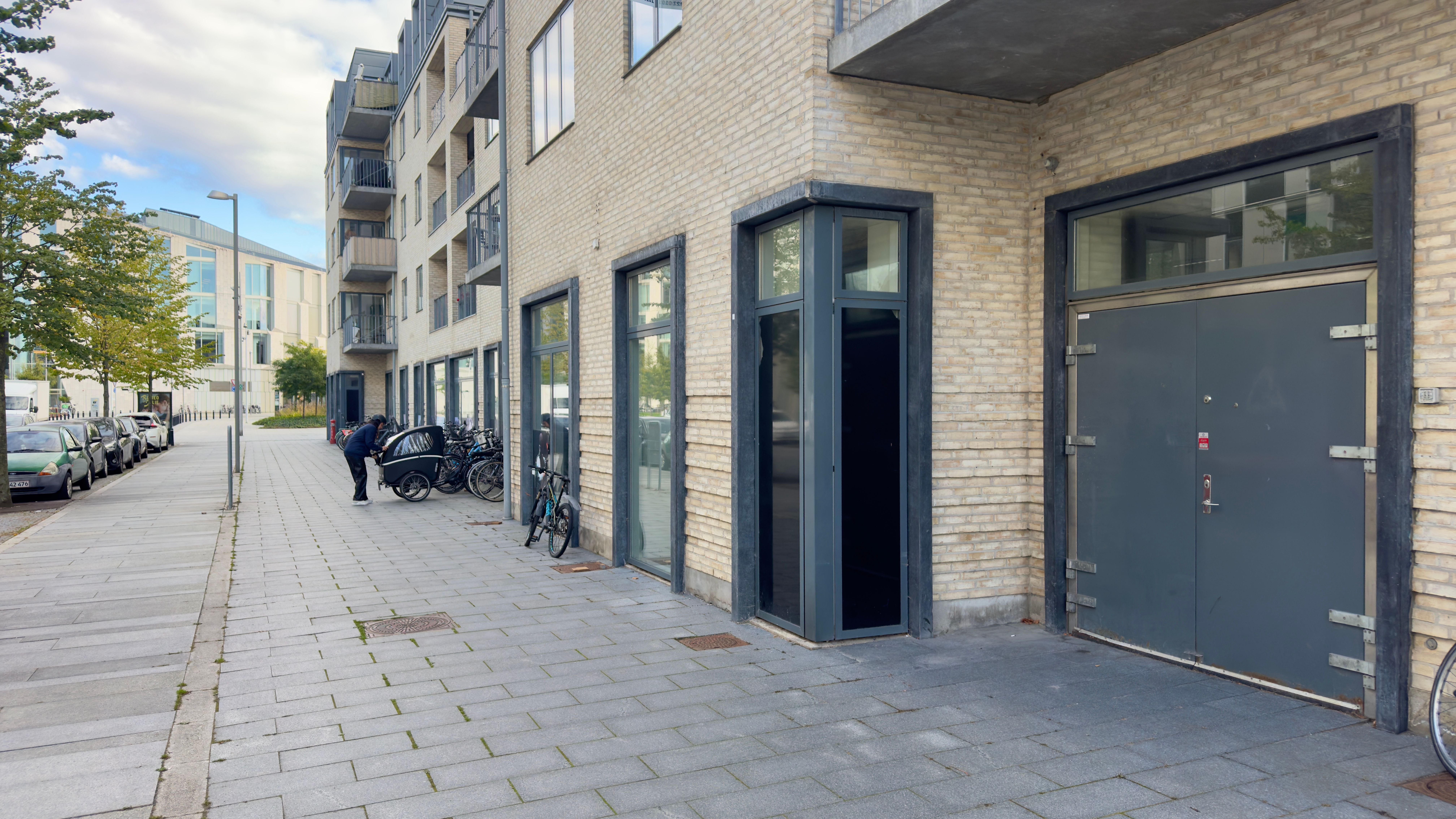 Lejemål med åbne døre til butik og garage med cykler parkeret udenfor og en person, der går forbi