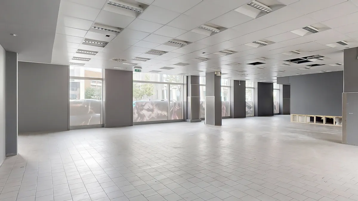 Store lokaler med hvidt gulv og loft og lyse glasruder med udsigt til vej og bygninger udenfor