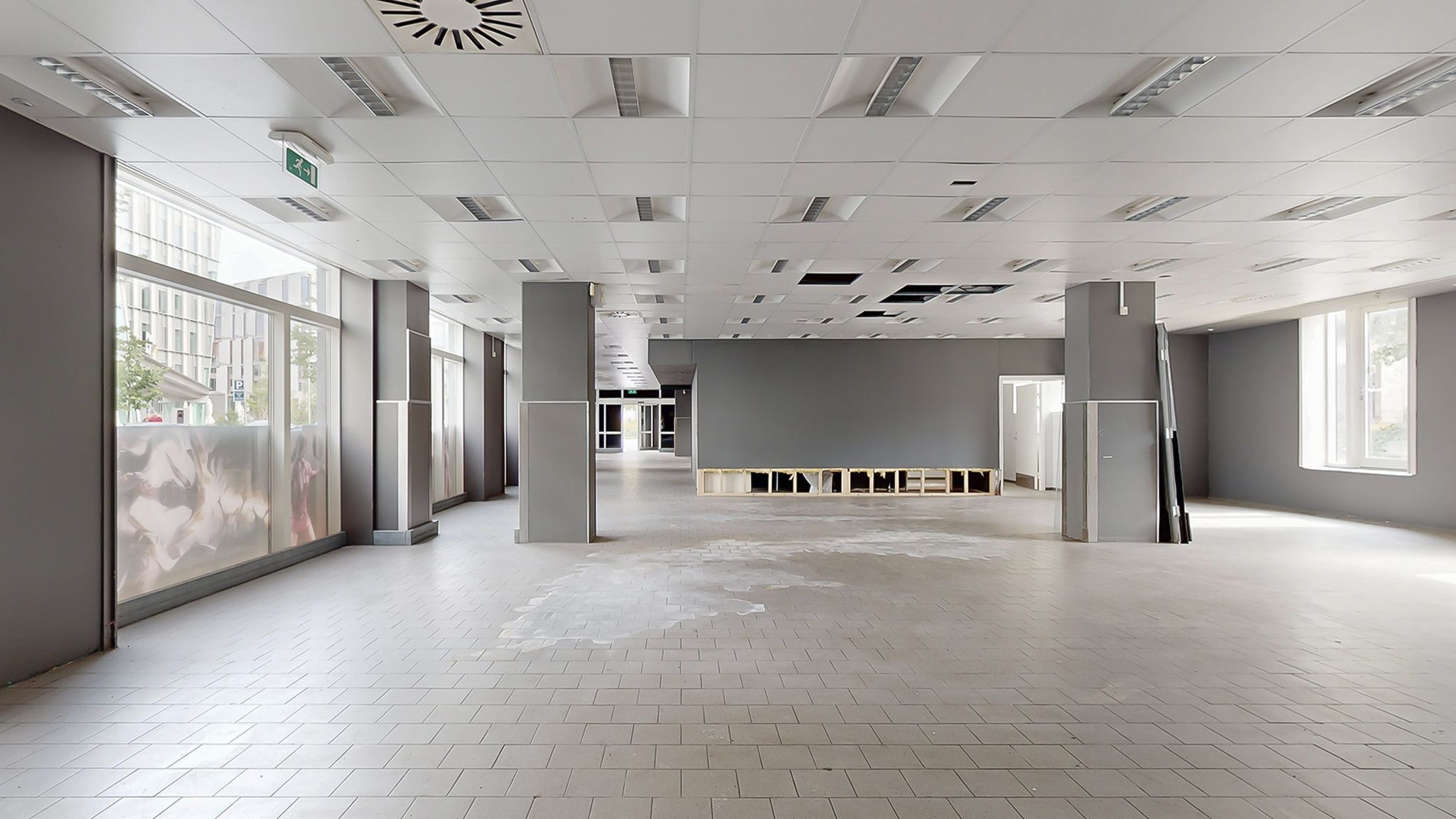 En stor tom forretningslokal med hvide gulvfliser, store vinduer og høje lofter med hængende ventiler