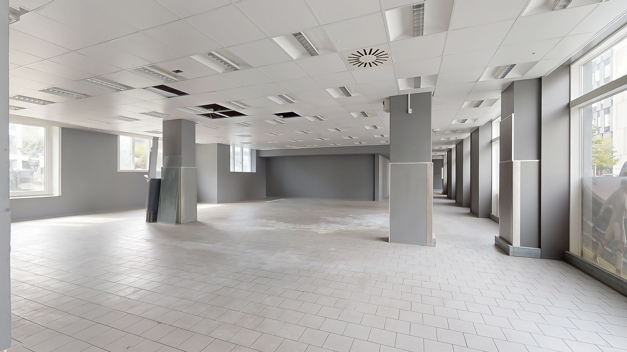 Moderne og lyse lokaler med hvide vægge, gulv og loft. To støtter og store vinduer med udsigt til byen.