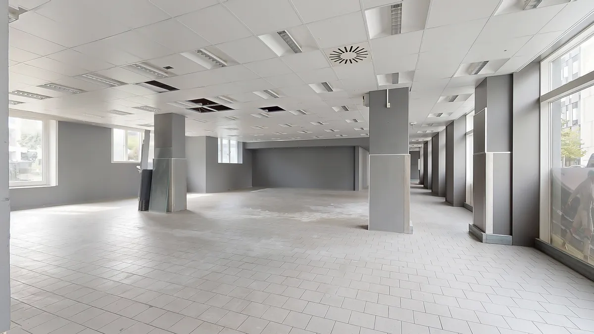 Moderne og lyse lokaler med hvide vægge, gulv og loft. To støtter og store vinduer med udsigt til byen.