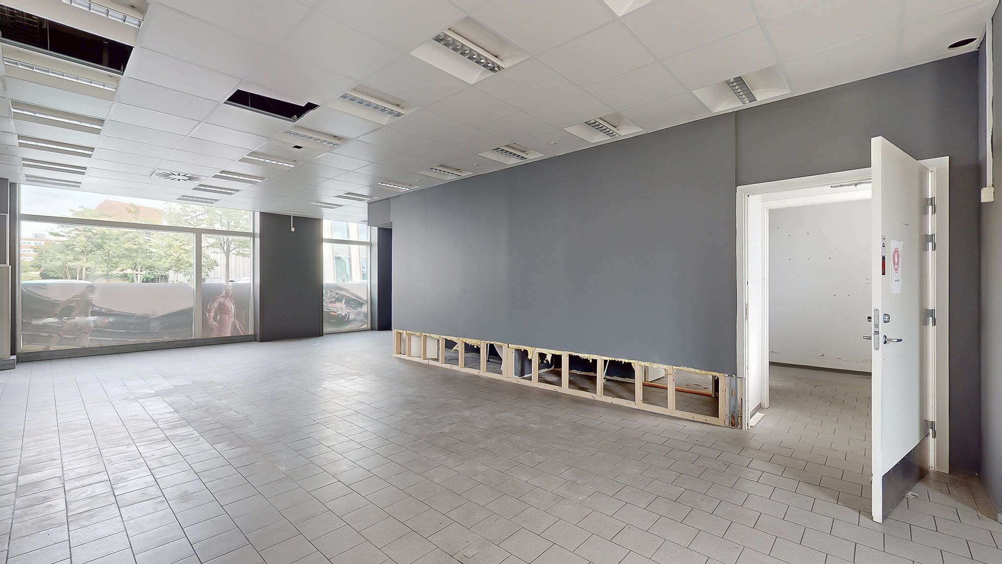 Store, lyse vinduer med udsigt til byen og biler parkeret udenfor. Store, hvide loftspaneler med integrerede lys. Et tømret