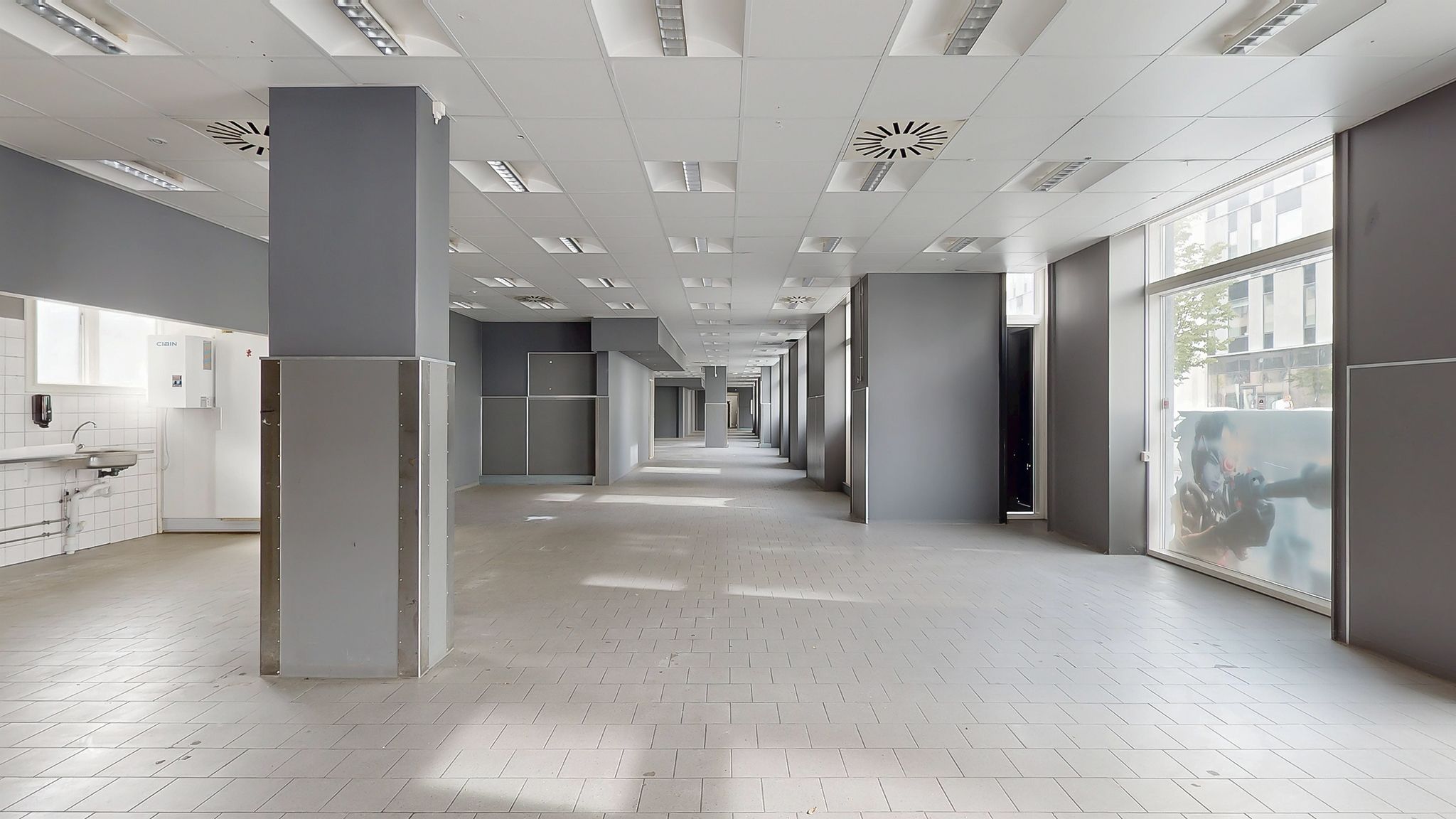 En tom gang med lysegult gulv og hvide vægge og loft. Det er en delvist tom og moderne indretning.