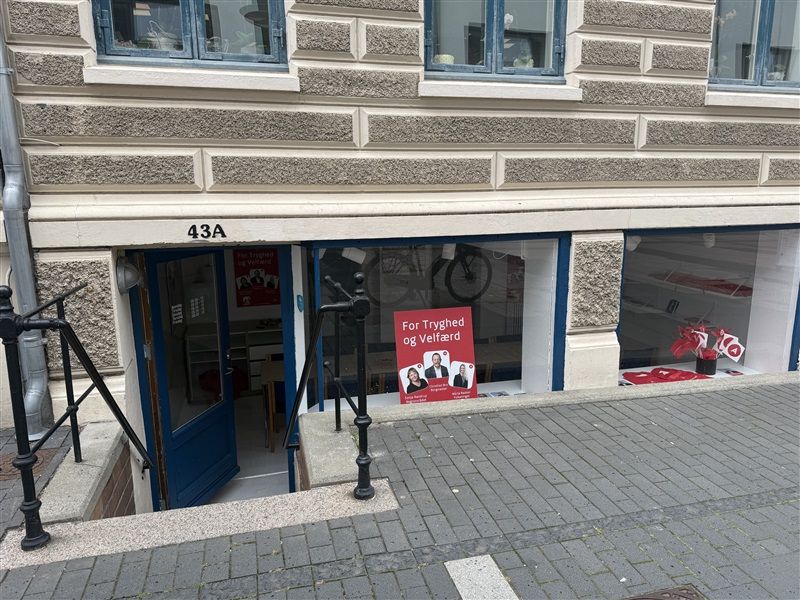Forretningslokale med nummer 43A i Fredericia, udstiller skilt med billeder af to personer og tekst på dansk