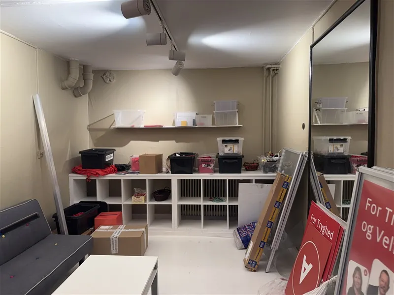 Lager med stol, sofa, hylder, kasser, kufferter, trækasser og skel i en rummelig værkstedslokal.