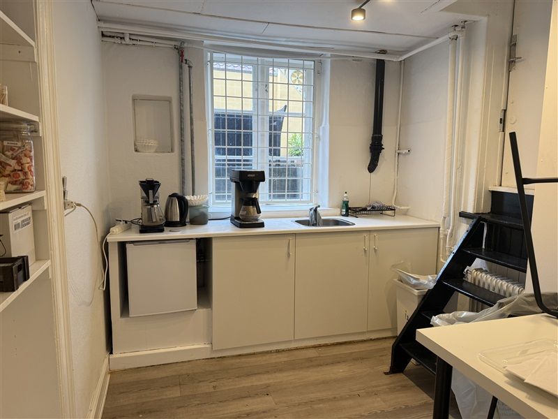 Køkken med lyse vægge, lysegrå køkkenskabe, lysegrå underskabe, lysegrå loftslampe og lysegrå loftslampe.