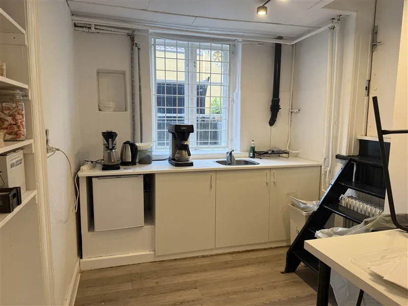 Køkken med lyse vægge, lysegrå køkkenskabe, lysegrå underskabe, lysegrå loftslampe og lysegrå loftslampe.