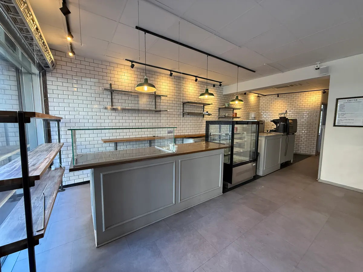 Et moderne køkken med rustfri stål og træelementer, og et udvalg af kager bag det glas og en kaffemaskine på højre side