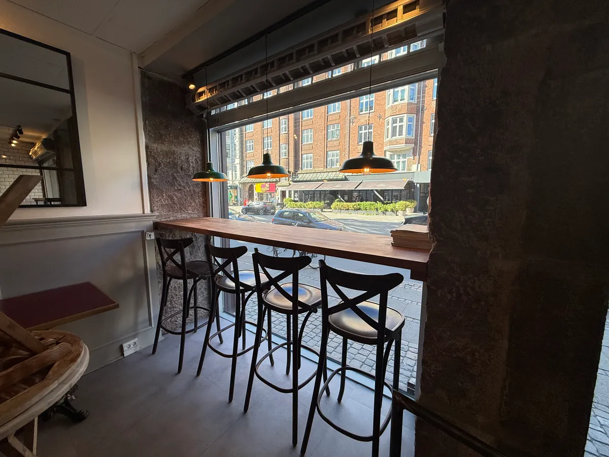 Bar med fire stole og lysekroner, der skuer ud på Østerbrogade med biler og bygninger i baggrunden