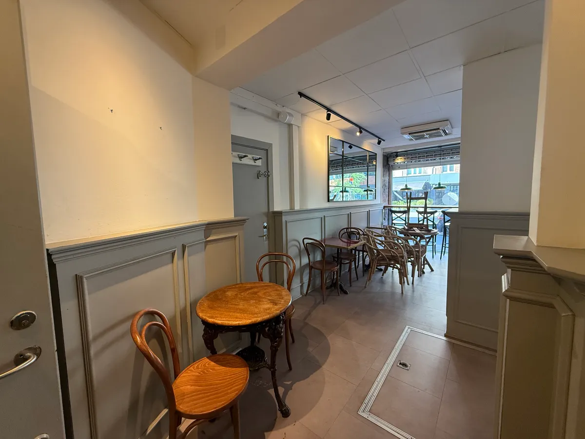 En lejemål i et tømmerkøkken med lyse vægge og gulv, stolpe og borde med stole samt et spejl og loftslampe.