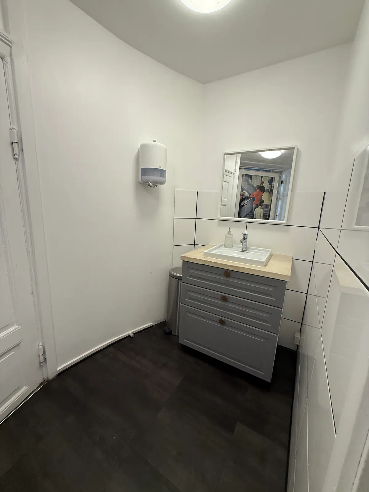 Lejlighed med toilet og spejl i hvidt og gråt. Toilet med vask og håndsæbe. Spejl med stribede vægge. Toiletpapirautomat ved